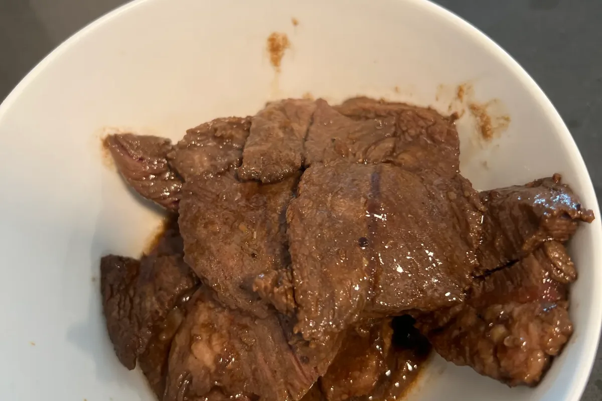 Seared beef strips, browned and glossy, resting in a white bowl.