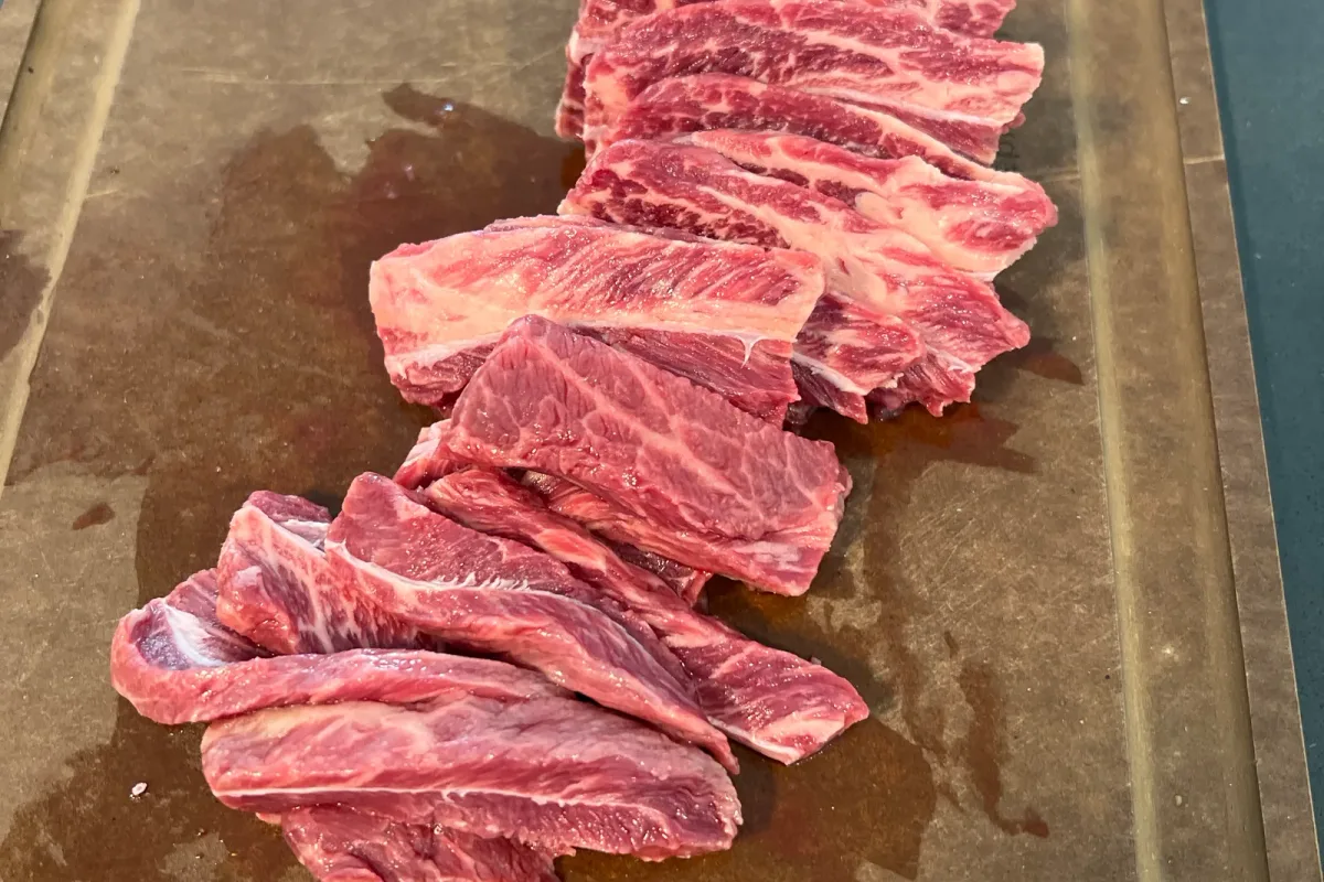 Raw flat iron steak sliced into thin strips against the grain.