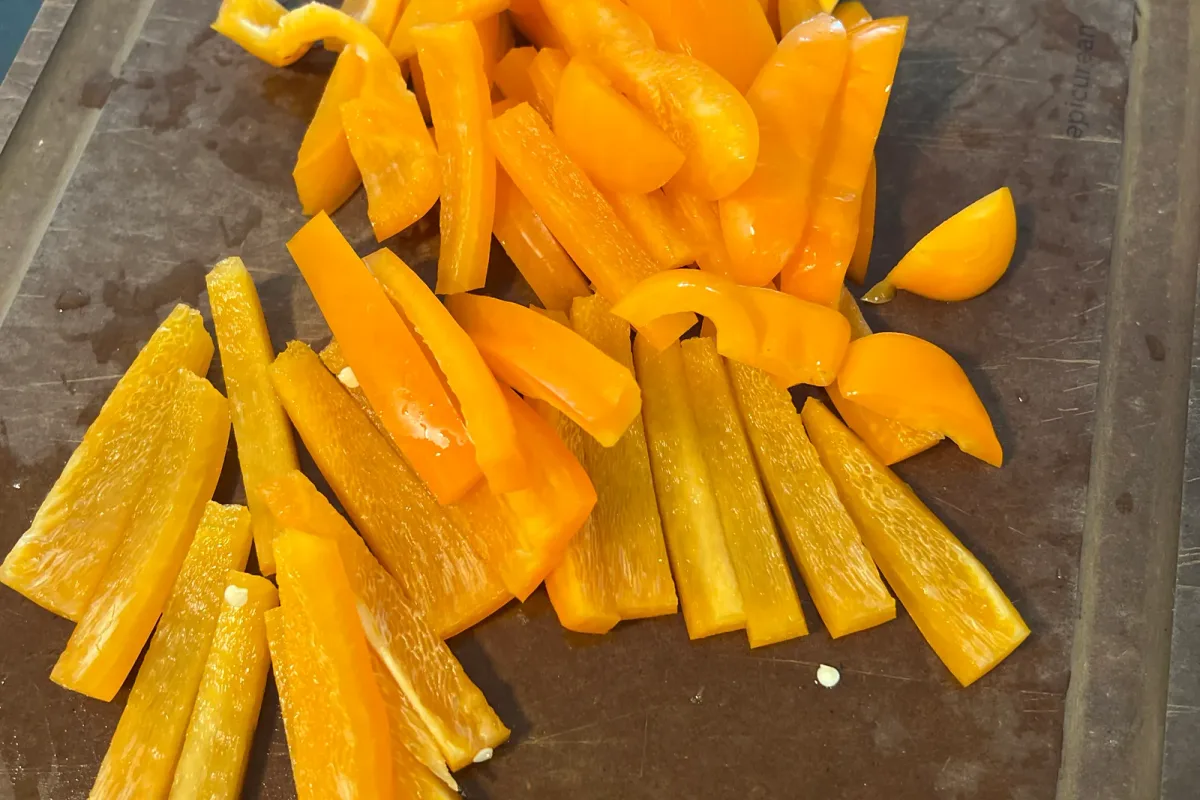 A larger pile of julienned orange bell pepper strips fanned out on the cutting board.