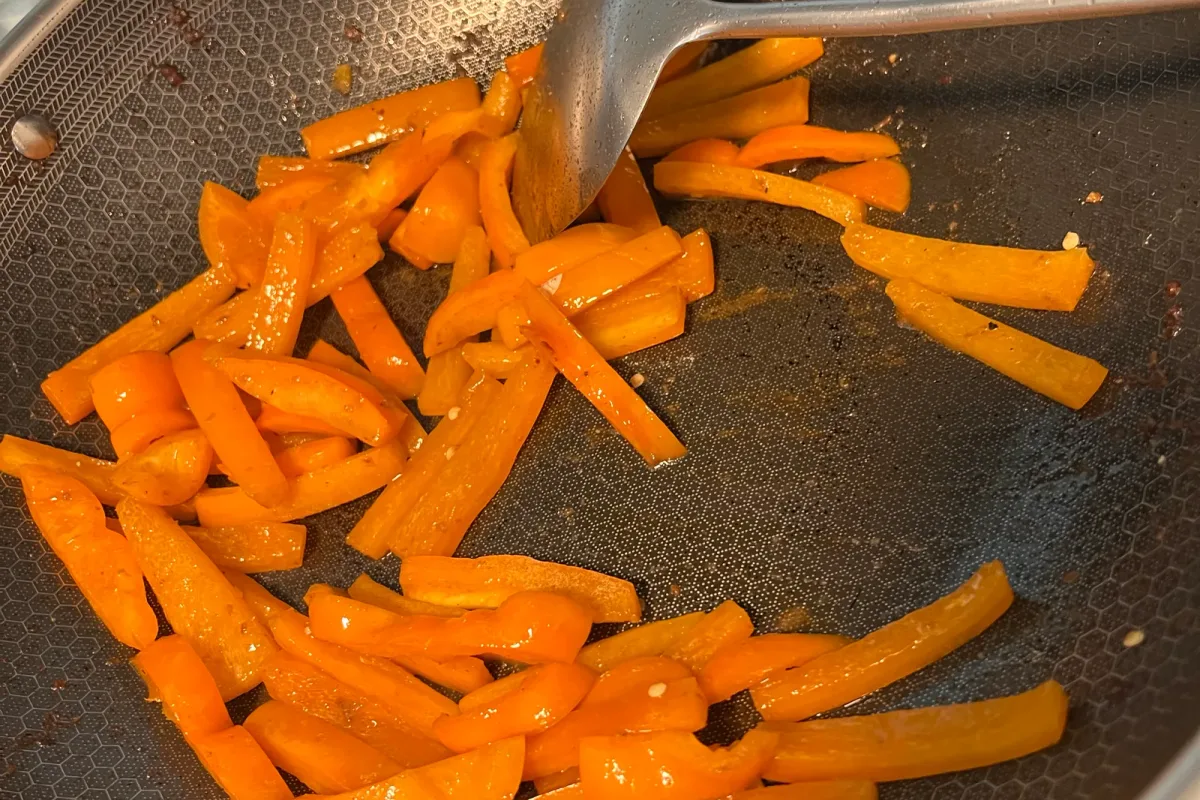Julienned orange peppers stir-frying in the wok, starting to blister and turn glossy.